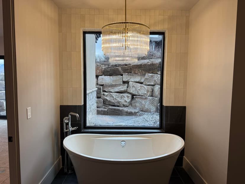 Modern bathroom featuring a freestanding bathtub, sleek chandelier, and stone window view.