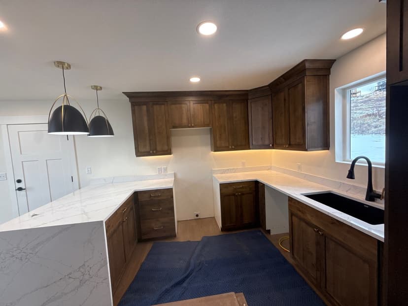 Modern kitchen with dark wood cabinets, white marble countertops, and black sink under natural light.
